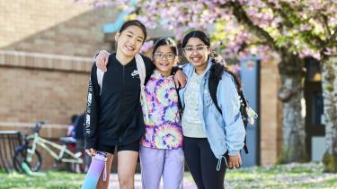 3 female elementary students in Abbotsford, BC underneath blossoming cherry trees